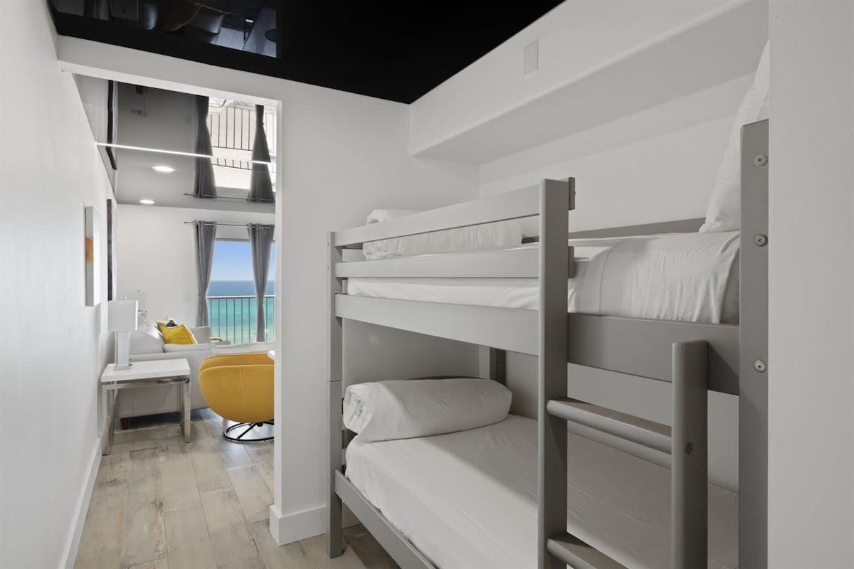 The Summit 702 – Bunk beds in a light room with ocean view, gray walls, and a yellow chair.