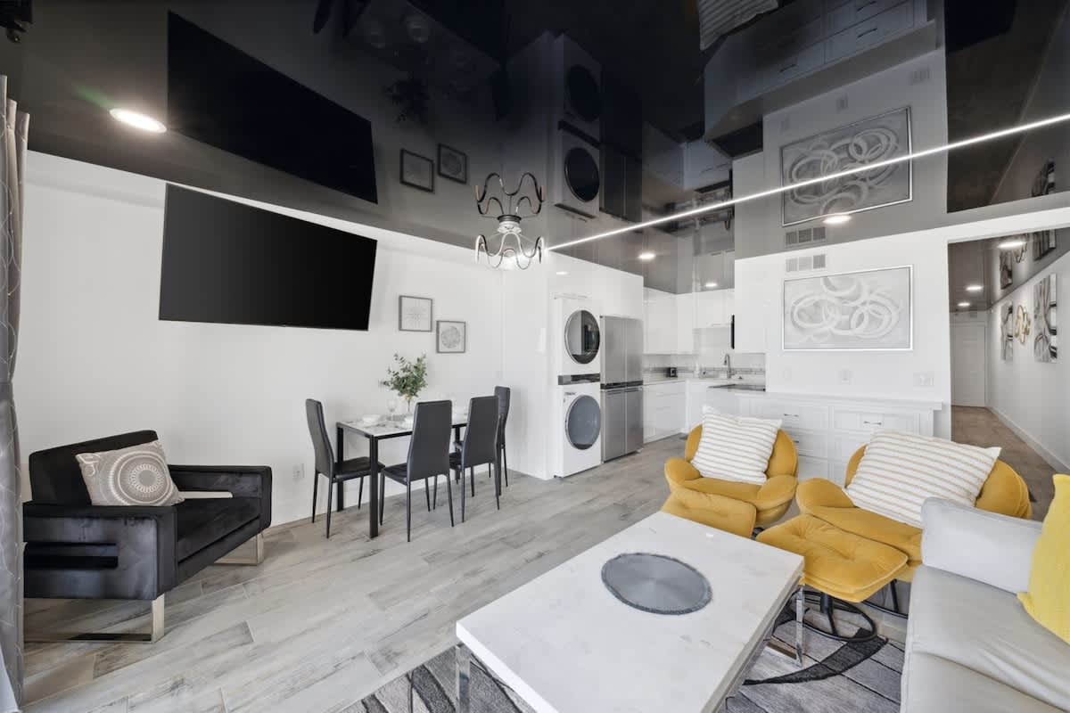 The Summit 702 – Modern living area with kitchen, dining table, dark sofa, yellow chairs, and large TV on the wall.