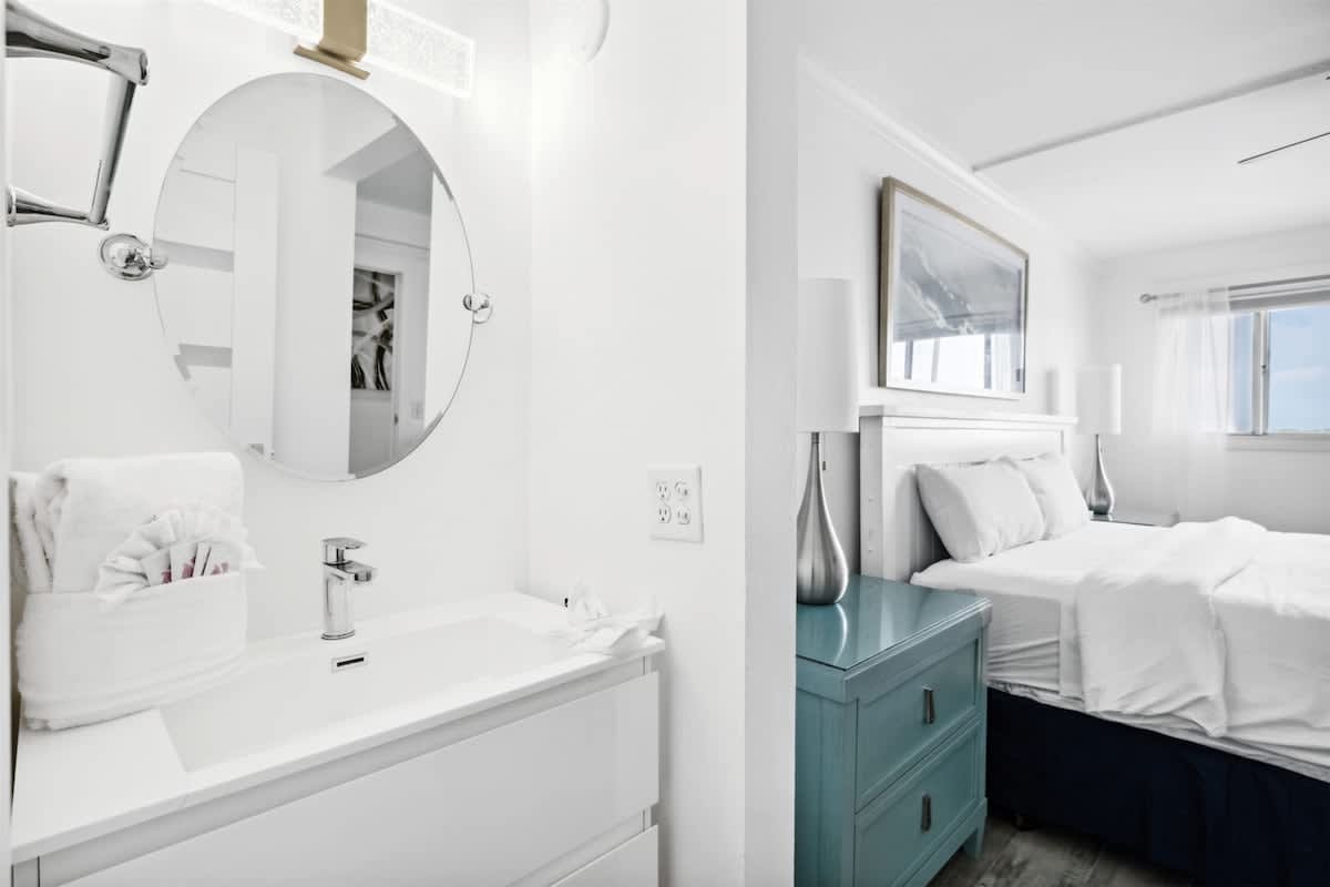 The Summit 702 – Bright bedroom and bathroom with a circular mirror, modern sink, and large window offering natural light.