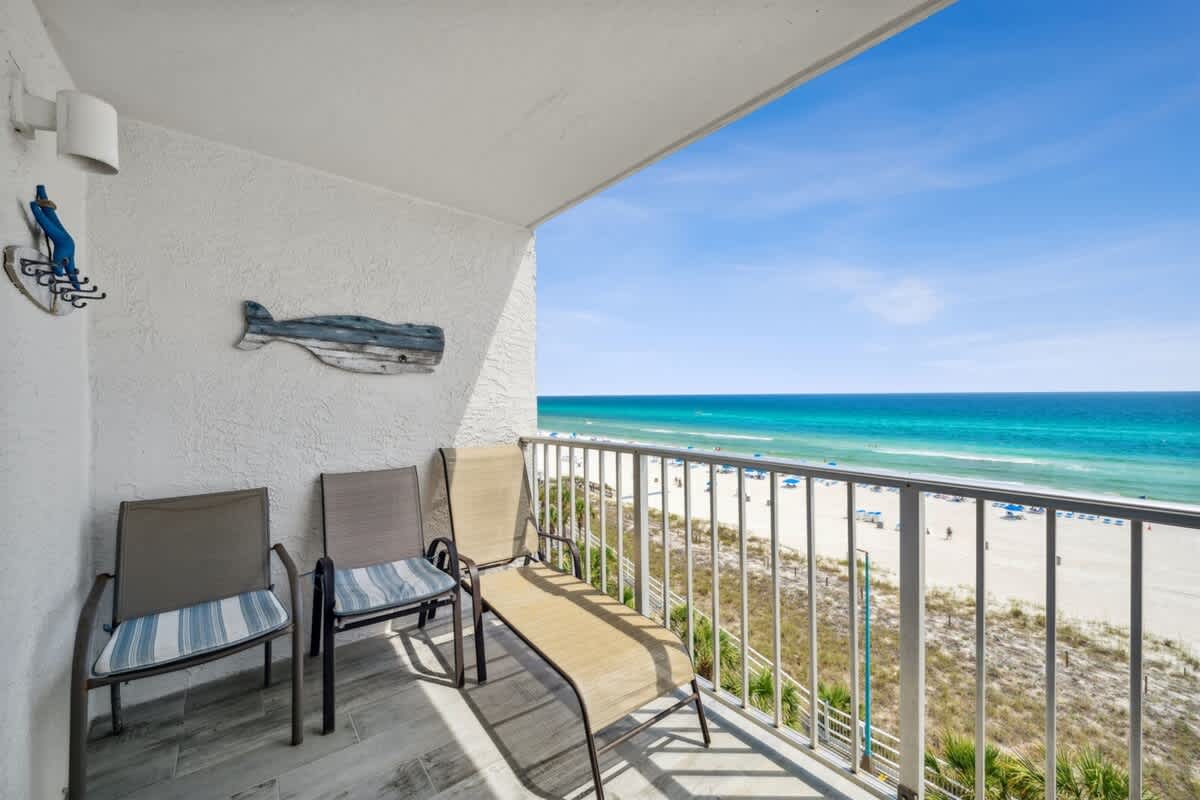 The Summit 702 – Balcony with three chairs and ocean view, overlooking sandy beach and umbrellas.