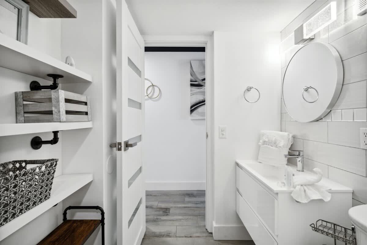 The Summit 702 – Modern bathroom with white cabinetry, circular mirror, and shelved storage space.