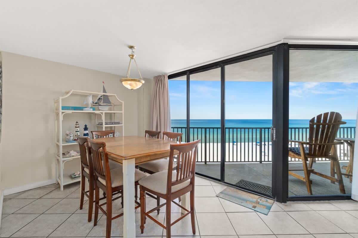 Aquavista 405e – Dining area with a wooden table, chairs, and floor-to-ceiling windows showing ocean view.