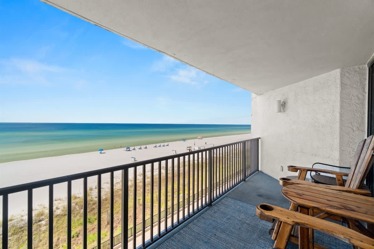 Aquavista 405e – Balcony view overlooking sandy beach and ocean with wooden chairs.
