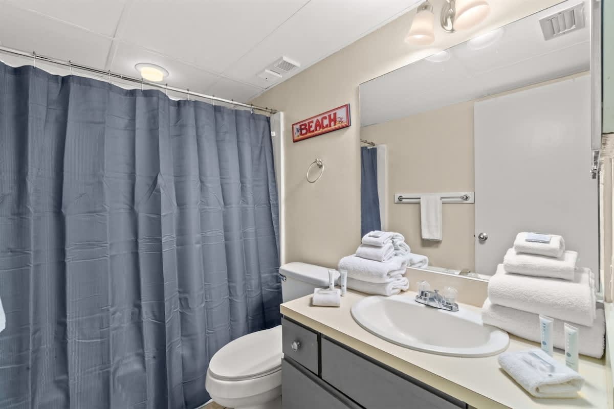 Aquavista 405e – Bathroom with a gray shower curtain, sink, toilet, towels, and lighted mirror.