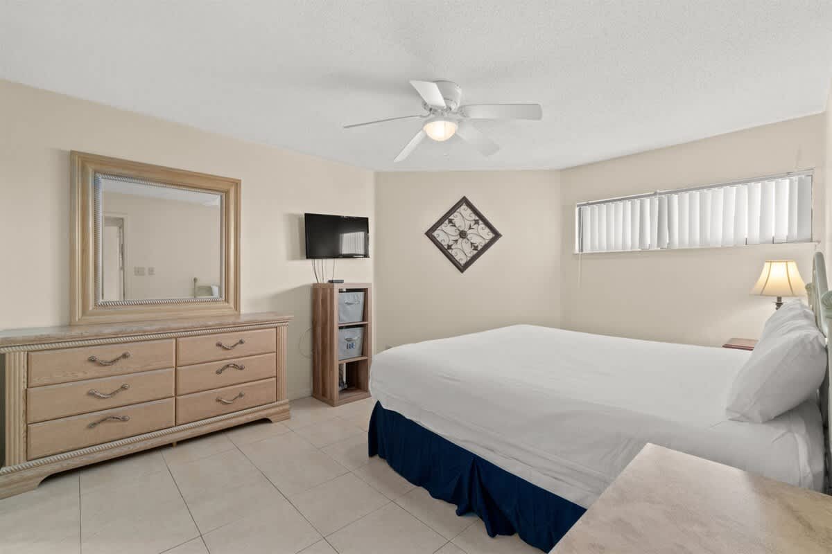 Aquavista 405e – Bedroom with a queen bed, dresser, TV, and large window with blinds.