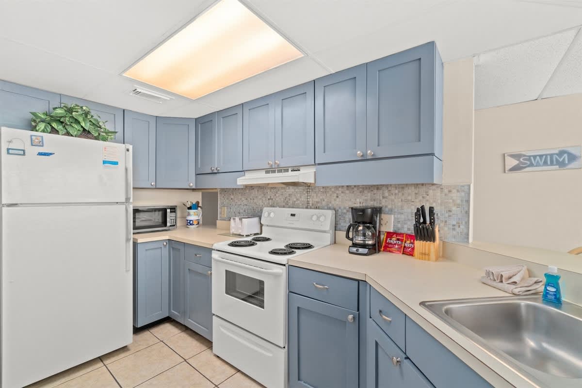 Aquavista 405e – Bright kitchen with blue cabinets, white appliances, countertop, and a coffee maker.