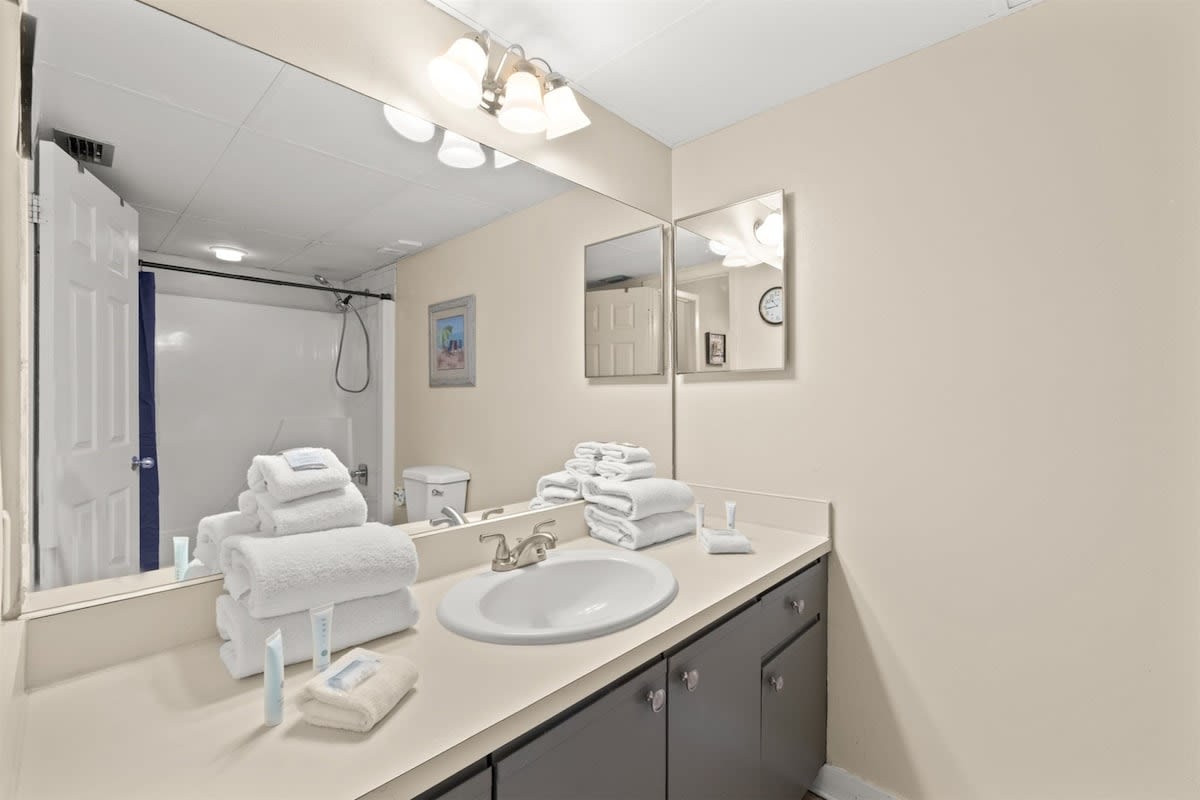 Aquavista 405e – Bathroom with a sink, large mirror, and stacked towels, featuring a shower and toilet in the background.