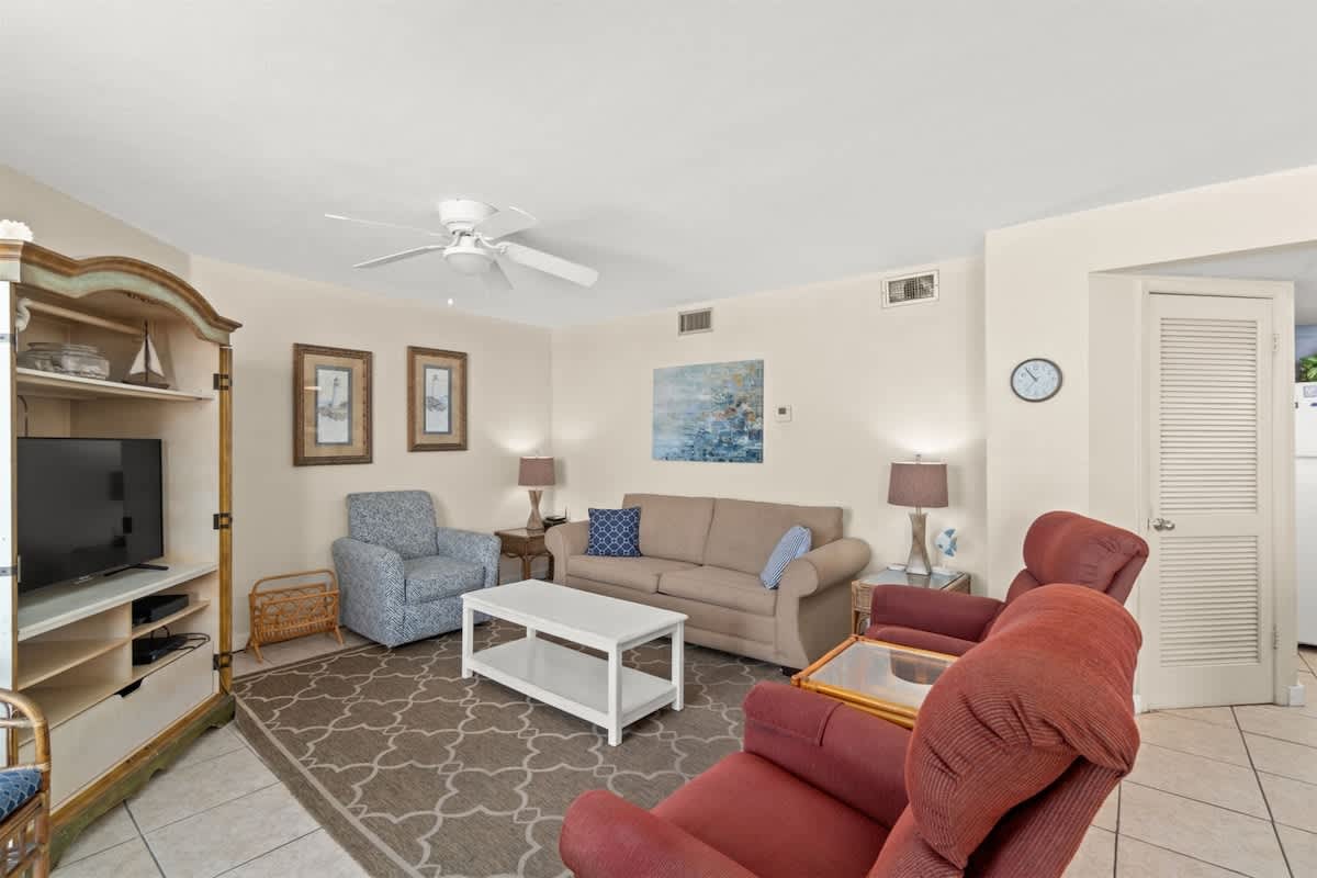 Aquavista 405e – Living room with beige couch, blue chair, TV, decorative art, and access to kitchen area.