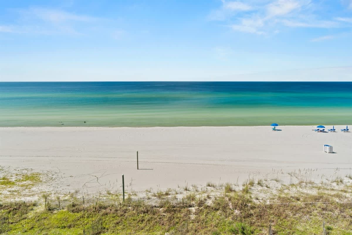 Aquavista 405e – View of a sandy beach with blue umbrellas and clear ocean waters under a bright sky.