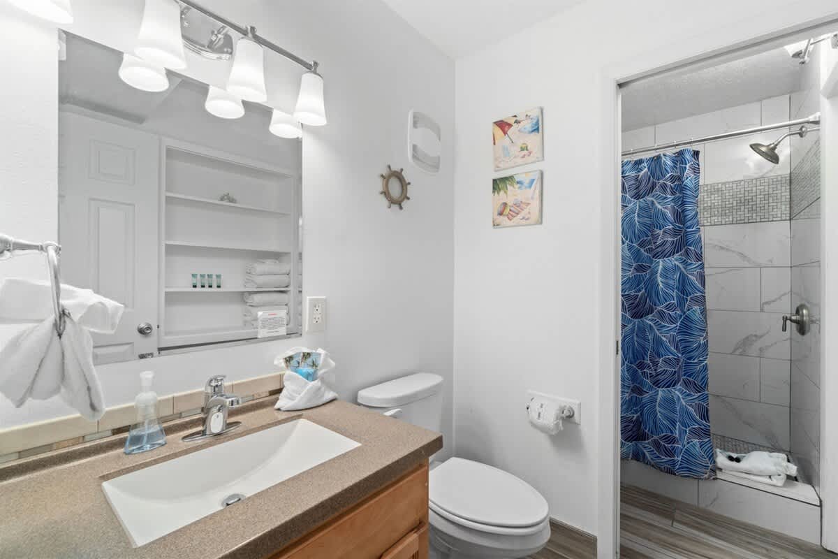 The Summit 1030 – Bathroom with sink, mirror, shower with blue curtain, and decorative beach-themed art.