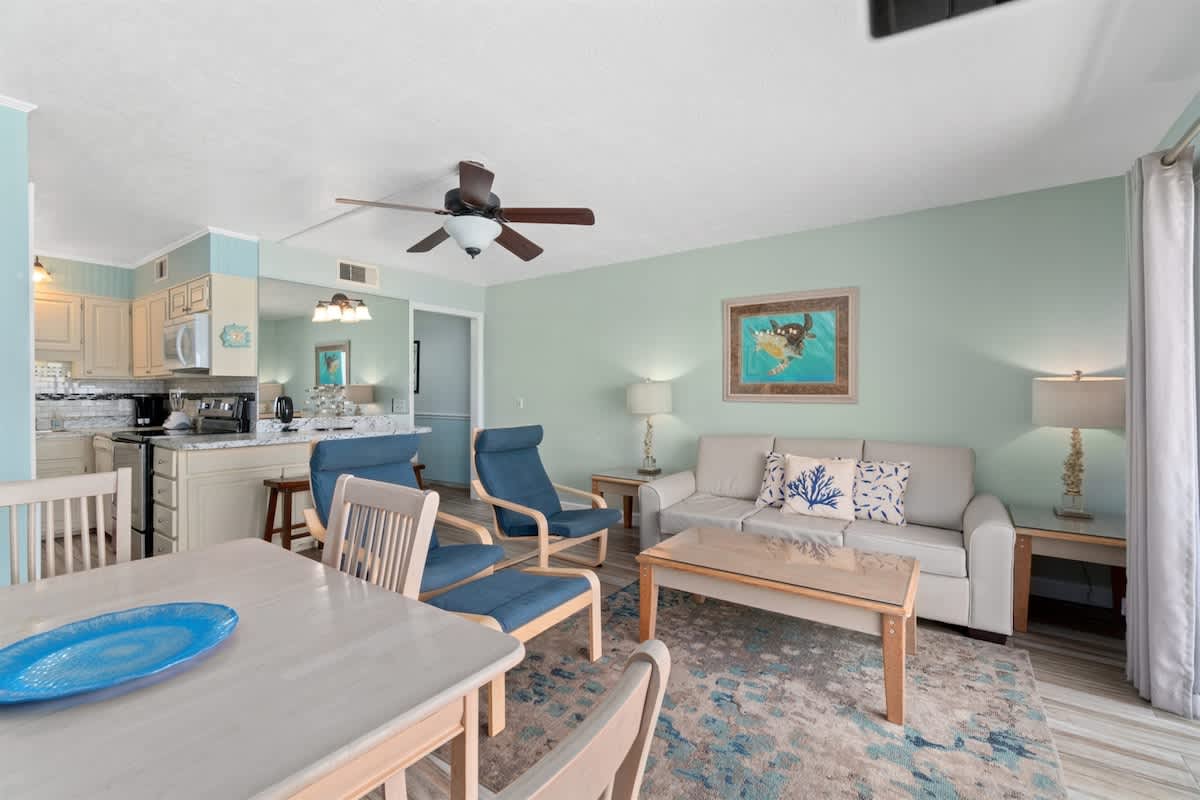 The Summit 1030 – Cozy living room with seating, dining area, and kitchen access; light blue walls and decorative accents.