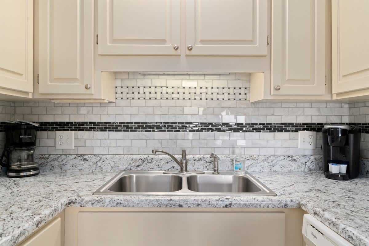 The Summit 1030 – Kitchen with granite countertops, double sink, coffee maker, and decorative tile backsplash.