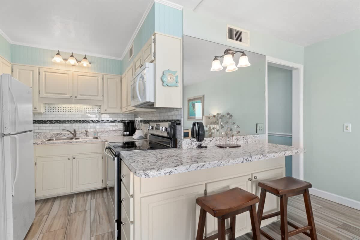 The Summit 1030 – Kitchen with granite countertops, stainless steel appliances, and two wooden stools at the bar area.