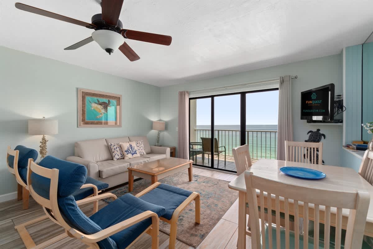 The Summit 1030 – Cozy living area with ocean view, balcony access, sofa, dining table, and blue accent chairs.