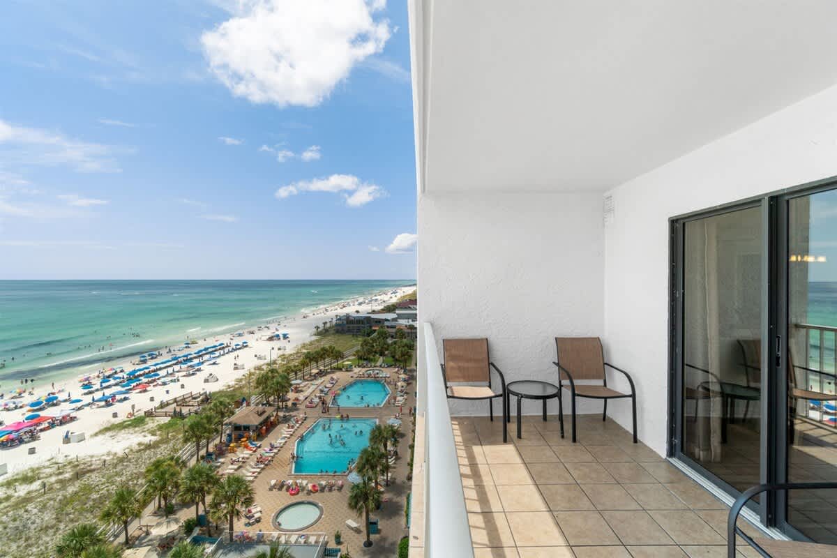The Summit 1030 – View from the balcony overlooking the beach, pools, and ocean with two chairs and a table.