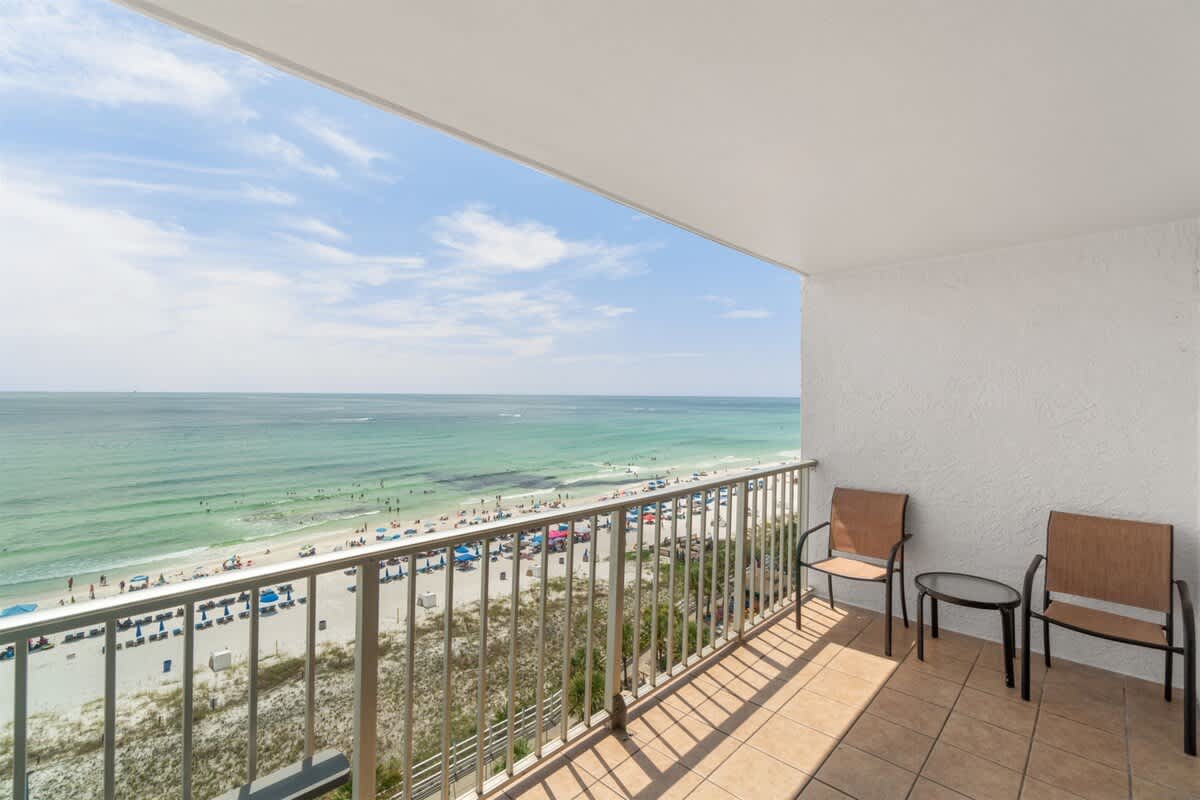 The Summit 1030 – Balcony view of beach and ocean with two chairs and a small table.