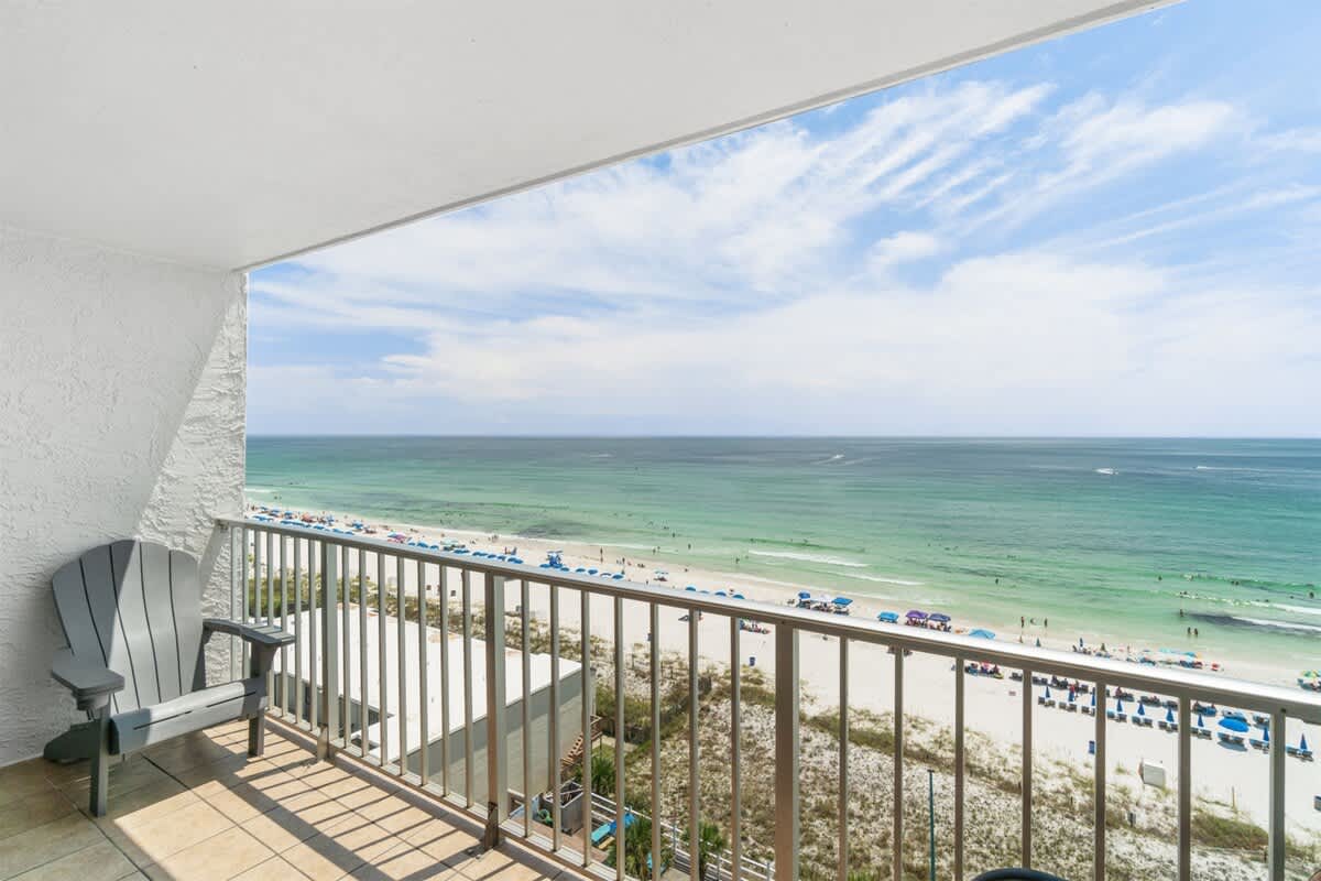 The Summit 1030 – Oceanview balcony with a gray chair, overlooking the beach and blue umbrellas.