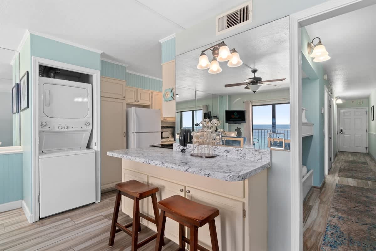 The Summit 1030 – Kitchen area with granite counter, bar stools, and view of ocean through large windows.