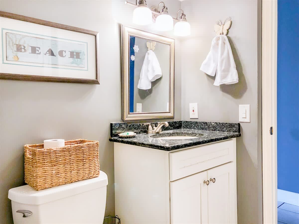 The Summit 611 – Bathroom with granite countertop, mirror, framed "BEACH" sign, and towels hanging on a white wall.