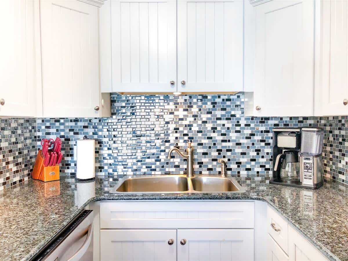 The Summit 611 – Modern kitchen with granite countertops, white cabinets, mosaic backsplash, double sink, and coffee maker.
