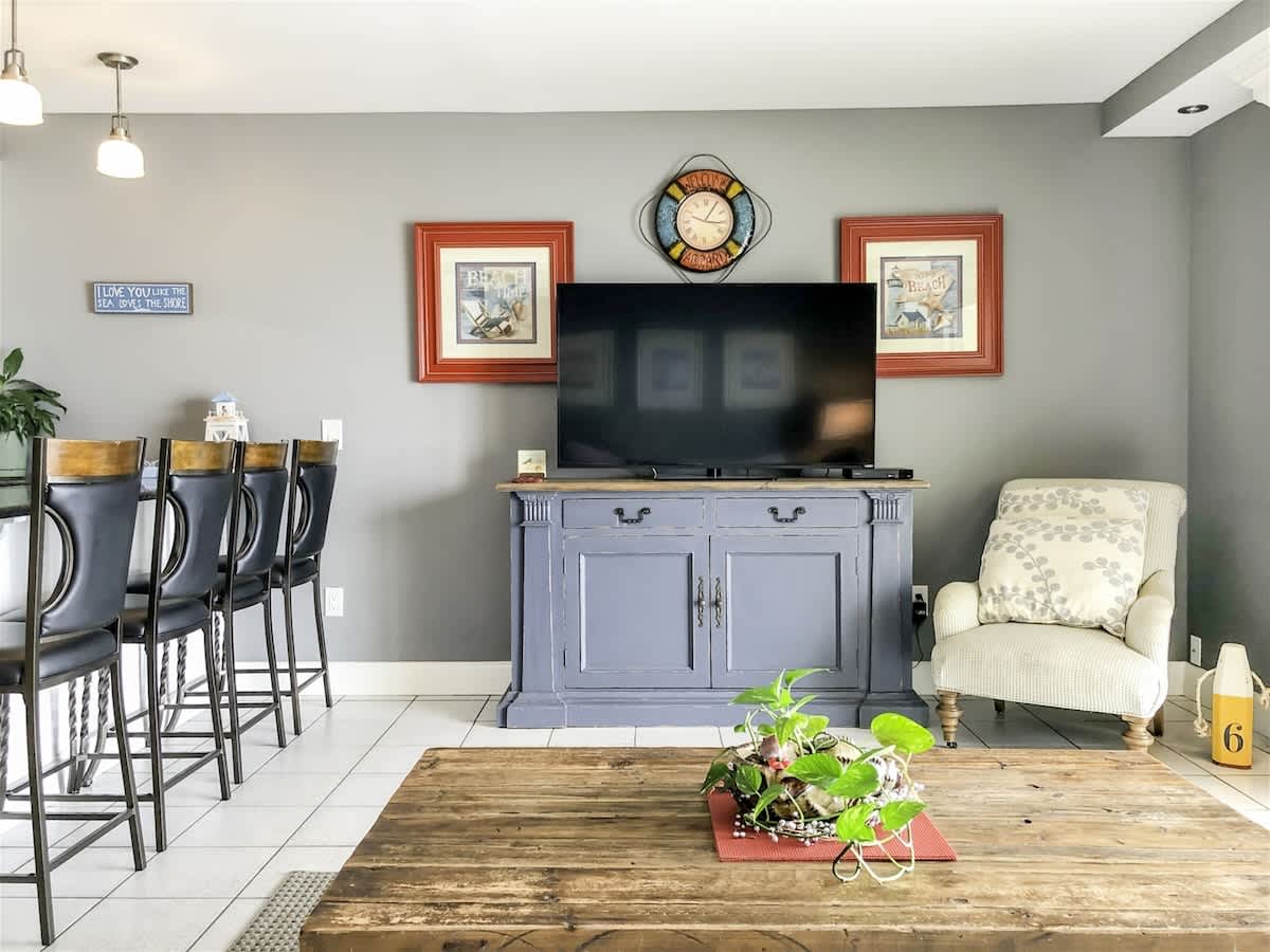 The Summit 611 – Living room with gray walls, TV, blue cabinet, wooden coffee table, bar stools, and armchair.