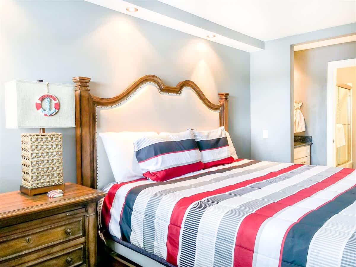 The Summit 611 – Cozy bedroom with a large bed, decorative lamp, and an adjoining bathroom area.