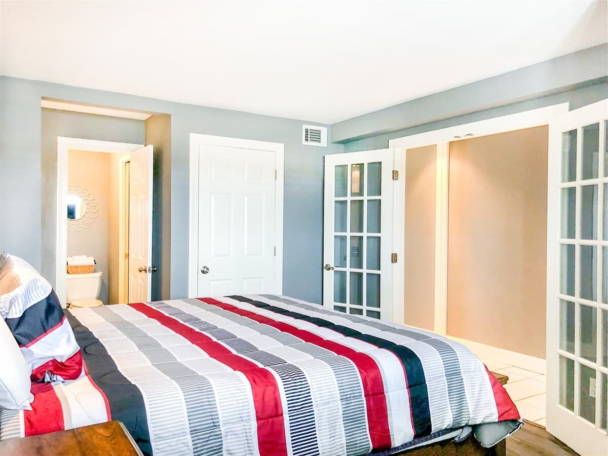 The Summit 611 – Bedroom with striped bedding, French doors, and doorway to a bathroom visible in the background.