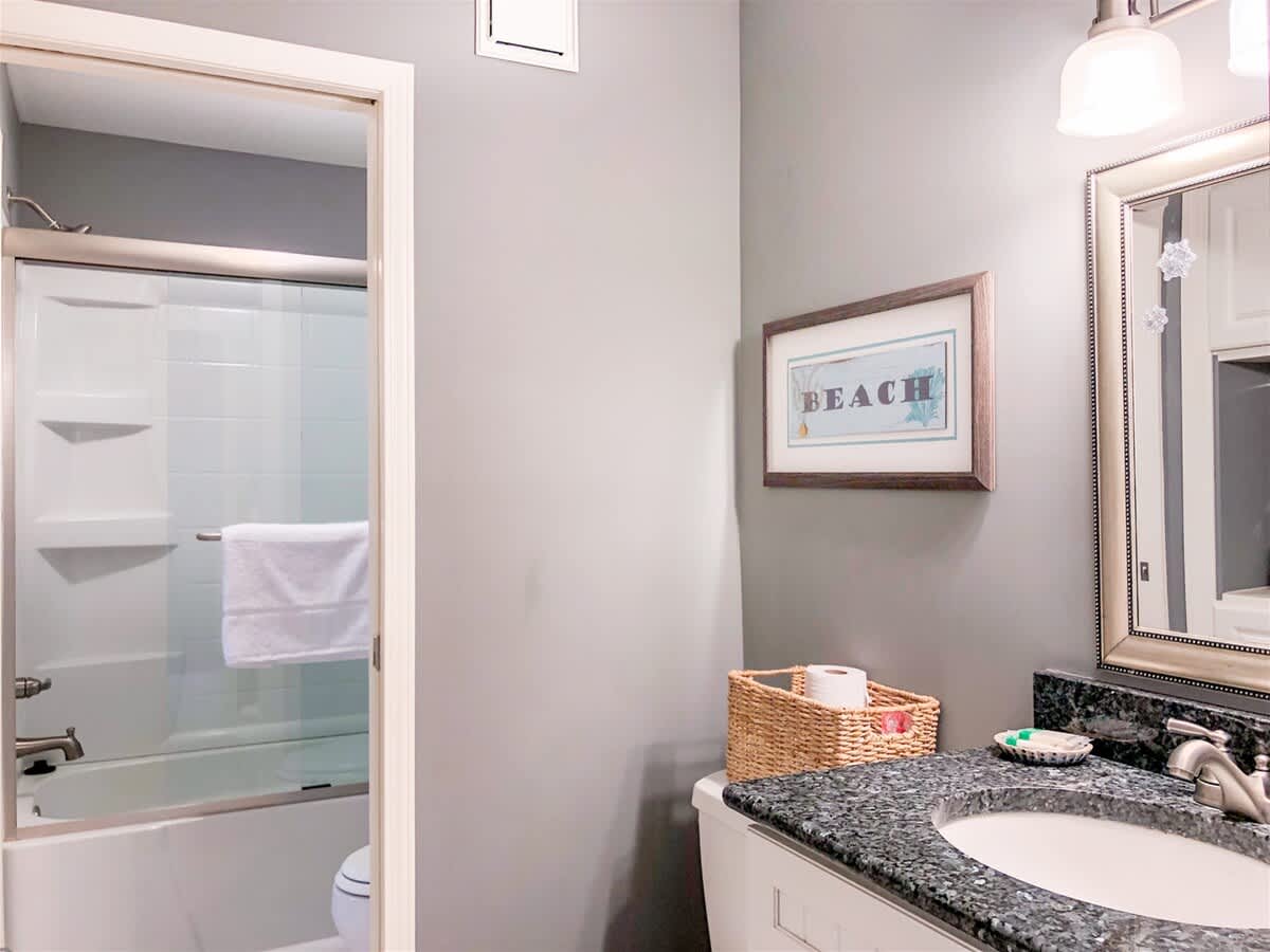 The Summit 611 – Bathroom featuring a shower, sink with dark countertop, and beach-themed wall art.