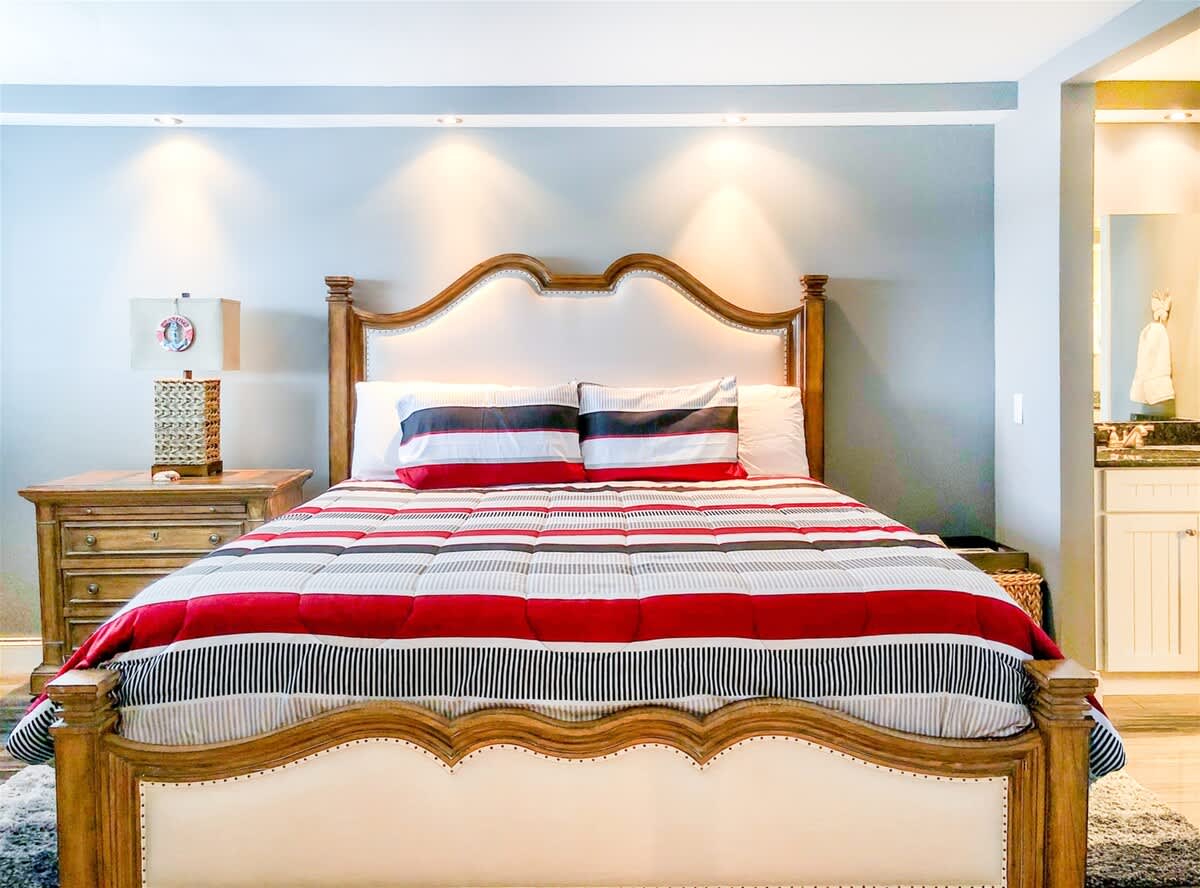 The Summit 611 – Bedroom with wooden bed frame, striped bedding, nightstand, and visible bathroom entrance.