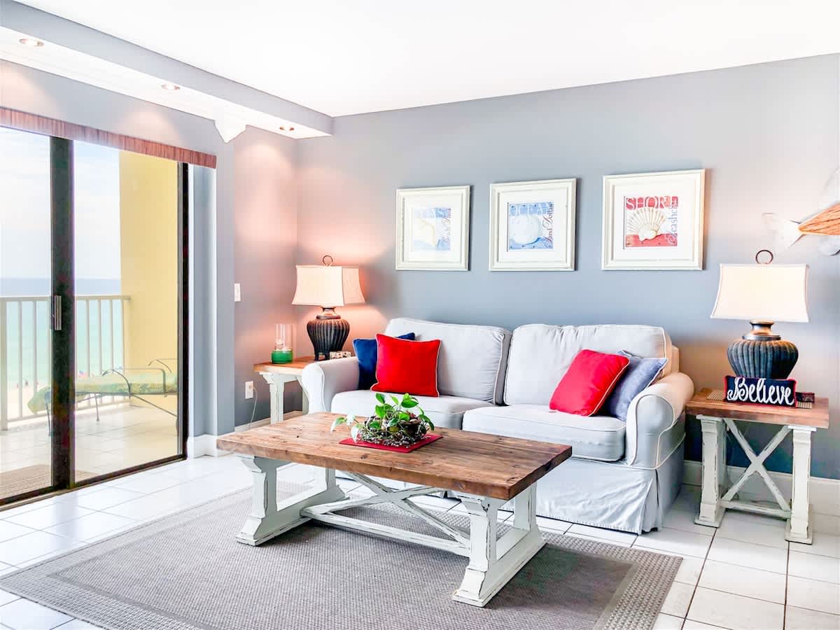 The Summit 611 – Cozy living room with a light gray sofa, wooden coffee table, lamps, and ocean view through sliding glass doors.