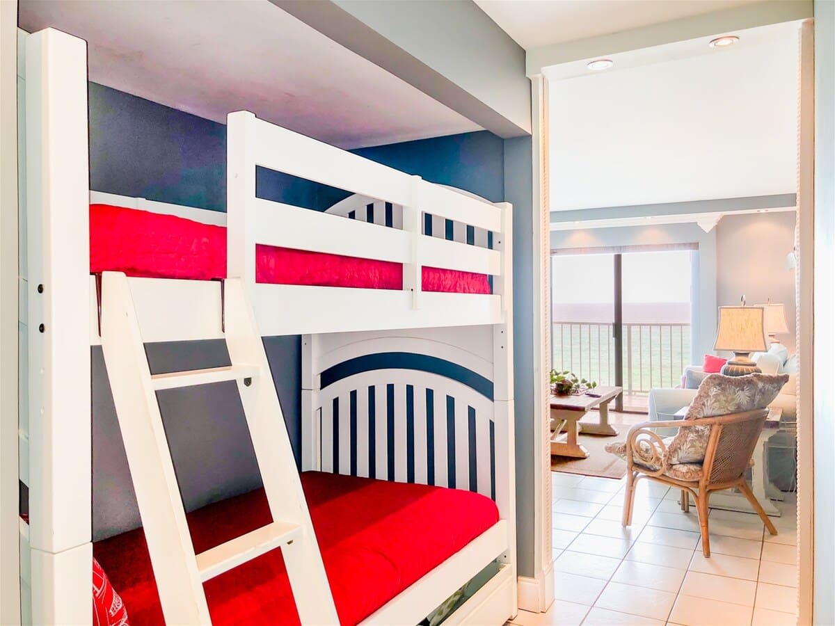 The Summit 611 – Bunk bed with red bedding, living area visible with ocean view and light furniture.