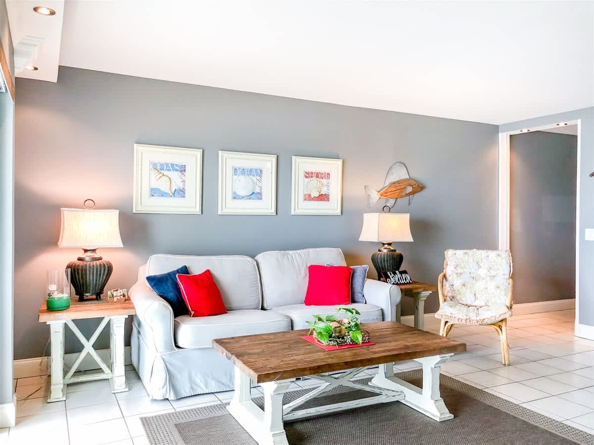 The Summit 611 – Living room with gray accent wall, sofa, decorative pillows, coffee table, two lamps, and beach-themed artwork.