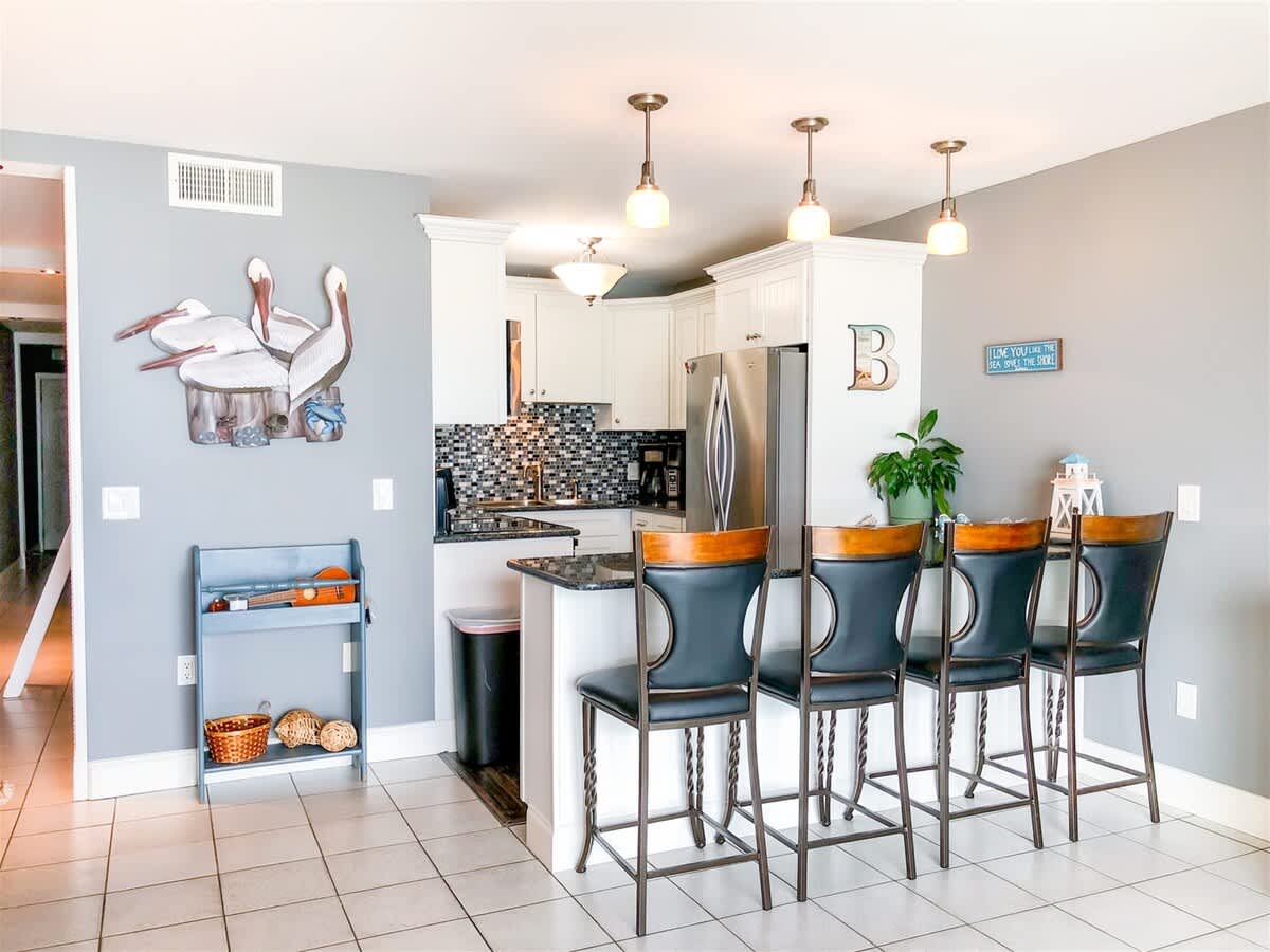 The Summit 611 – Contemporary kitchen with black bar stools, mosaic backsplash, and decorative pelican wall art.