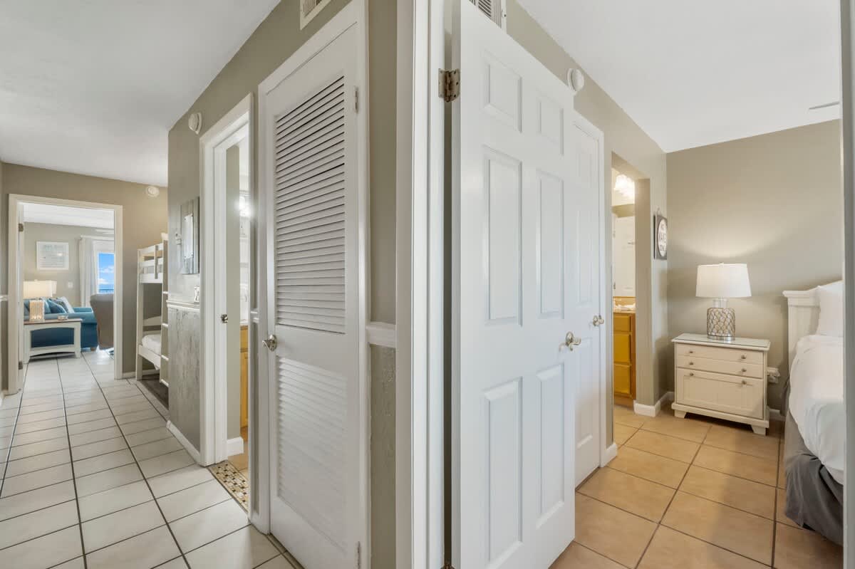 The Summit 1128 – Hallway view with tiled floor, doors to bedrooms and bathroom, light-colored walls, and lamp on nightstand.