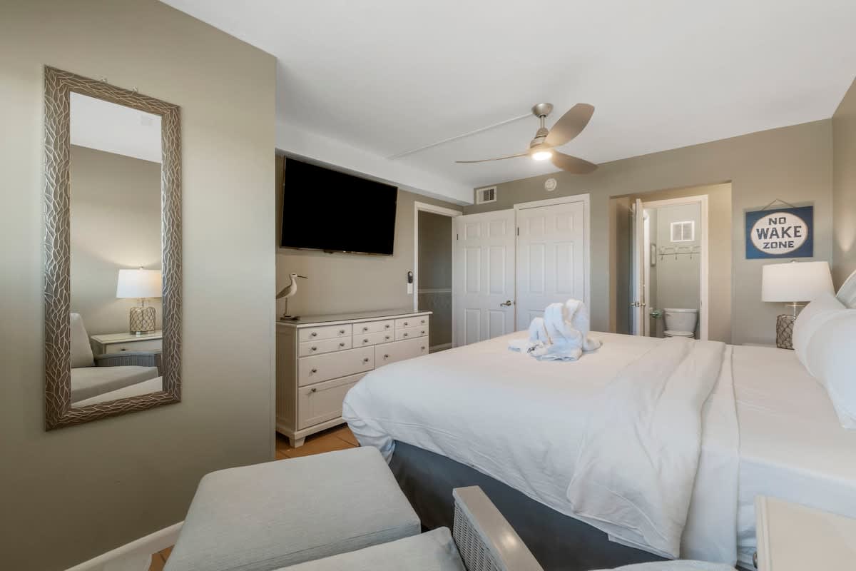 The Summit 1128 – Cozy bedroom with a queen bed, dresser, TV, sitting area, and en-suite bathroom access.