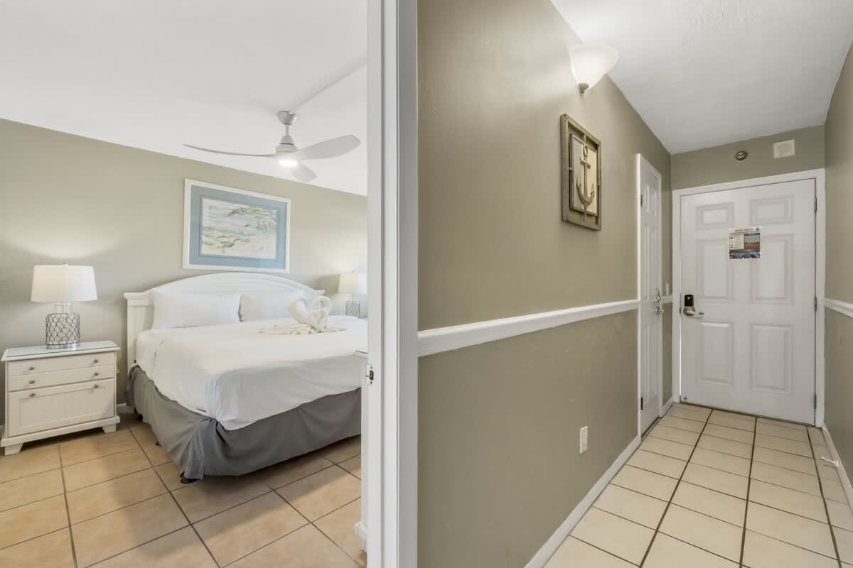 The Summit 1128 – Hallway view into a bedroom with a king bed, lamps, and decorative art on the walls.