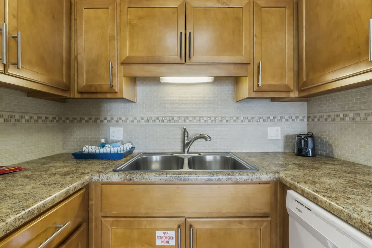 The Summit 1128 – Kitchen with wooden cabinets, granite countertops, double sink, and small appliances.