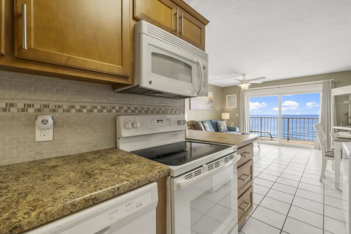 The Summit 1128 – Kitchen area with granite countertops, white appliances, and ocean view through large sliding glass doors.