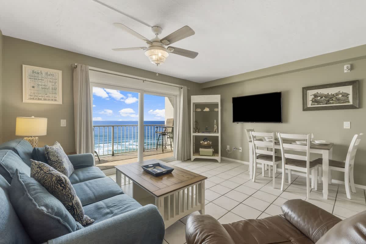 The Summit 1128 – Living room with ocean view, couch, dining table, and large windows opening to a balcony.