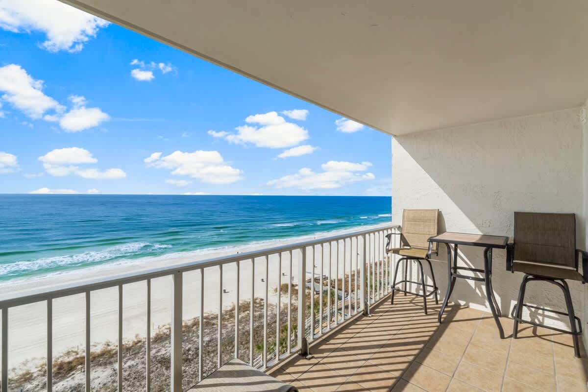 The Summit 1128 – Balcony view with two chairs overlooking the beach and ocean under a blue sky.
