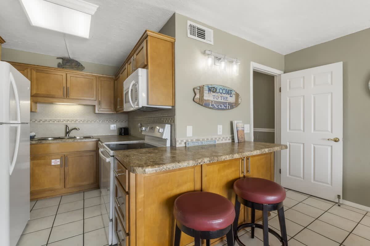 The Summit 1128 – Kitchen with wooden cabinets, granite countertops, stainless appliances, and two stools at a breakfast bar.
