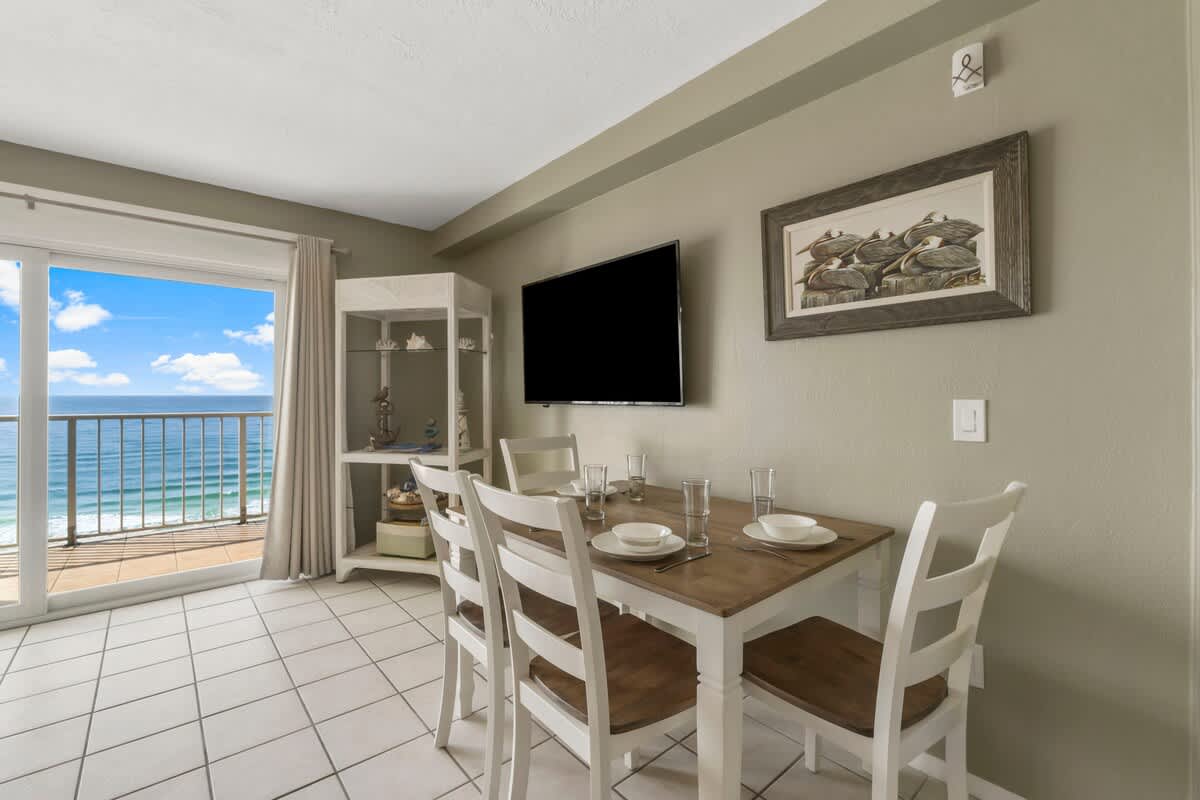 The Summit 1128 – Dining area with table, four chairs, and ocean view through sliding glass doors.
