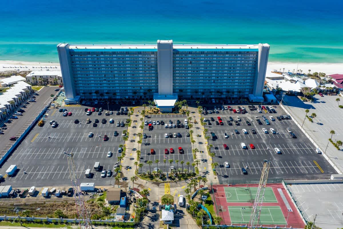 The Summit 1128 – Aerial view of a large beachfront hotel with parking lots and a tennis court in the foreground.