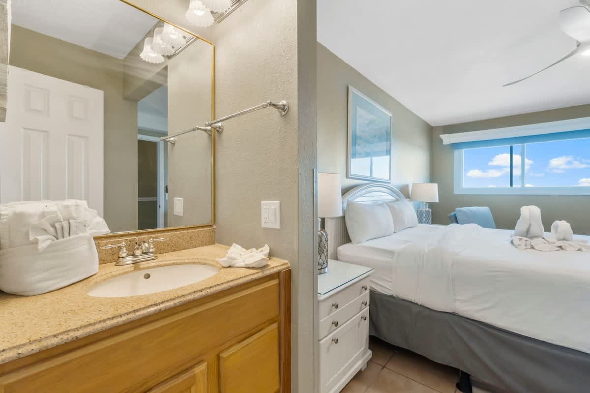 The Summit 1128 – Bedroom with a bed, nightstands, window view, and adjoining bathroom with sink and mirror.