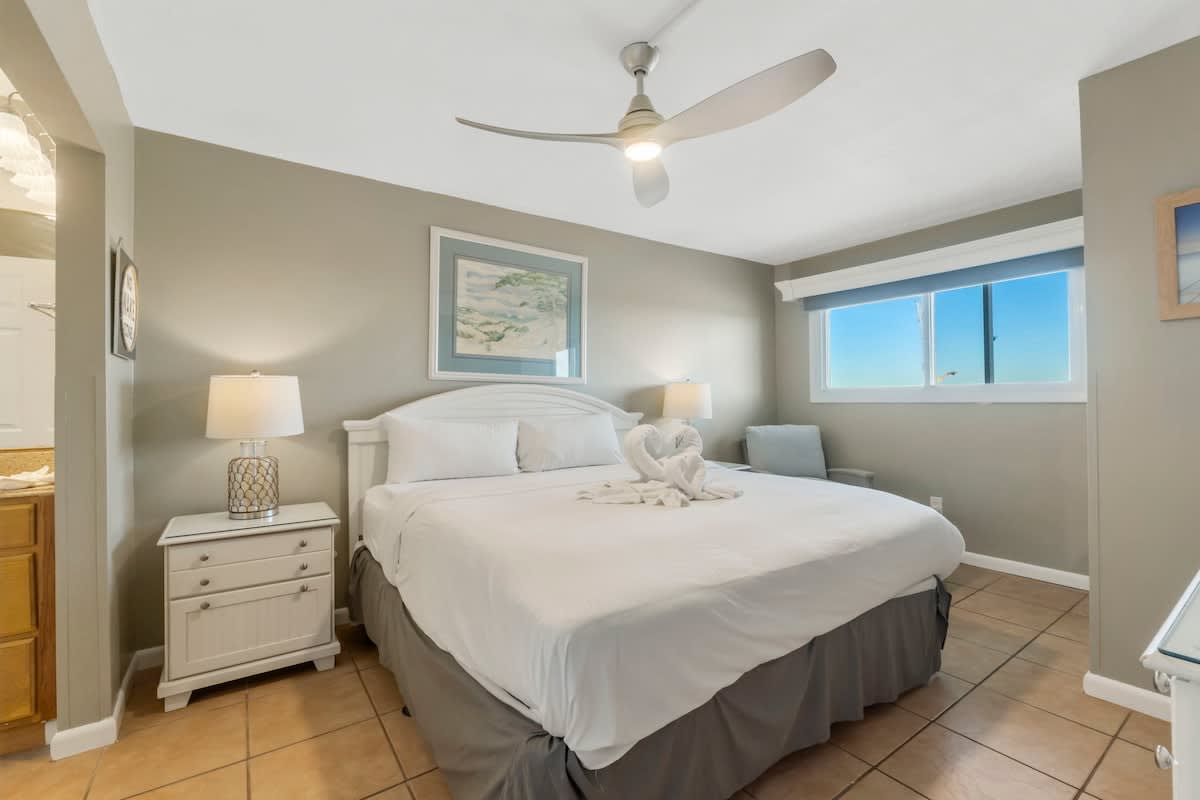 The Summit 1128 – King bedroom with white linens, side tables, window view, and towels arranged in heart shape.