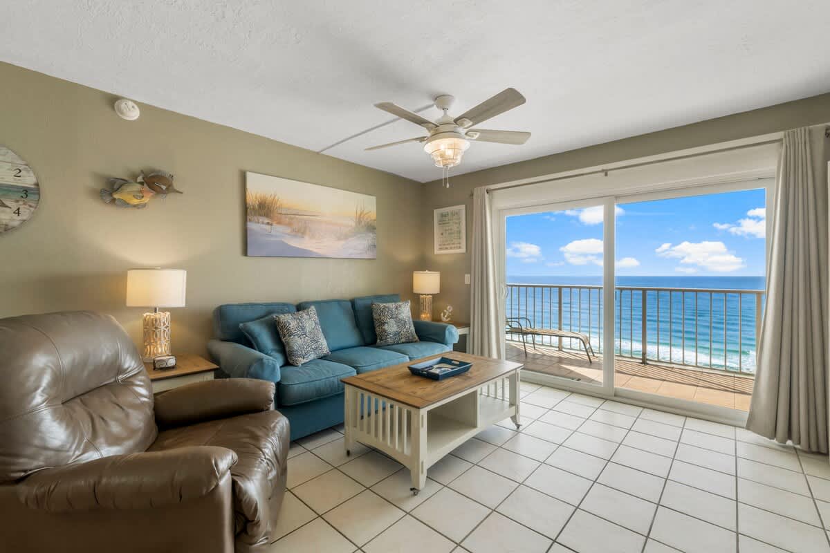 The Summit 1128 – Living room with blue sofa, leather chair, and ocean view balcony.