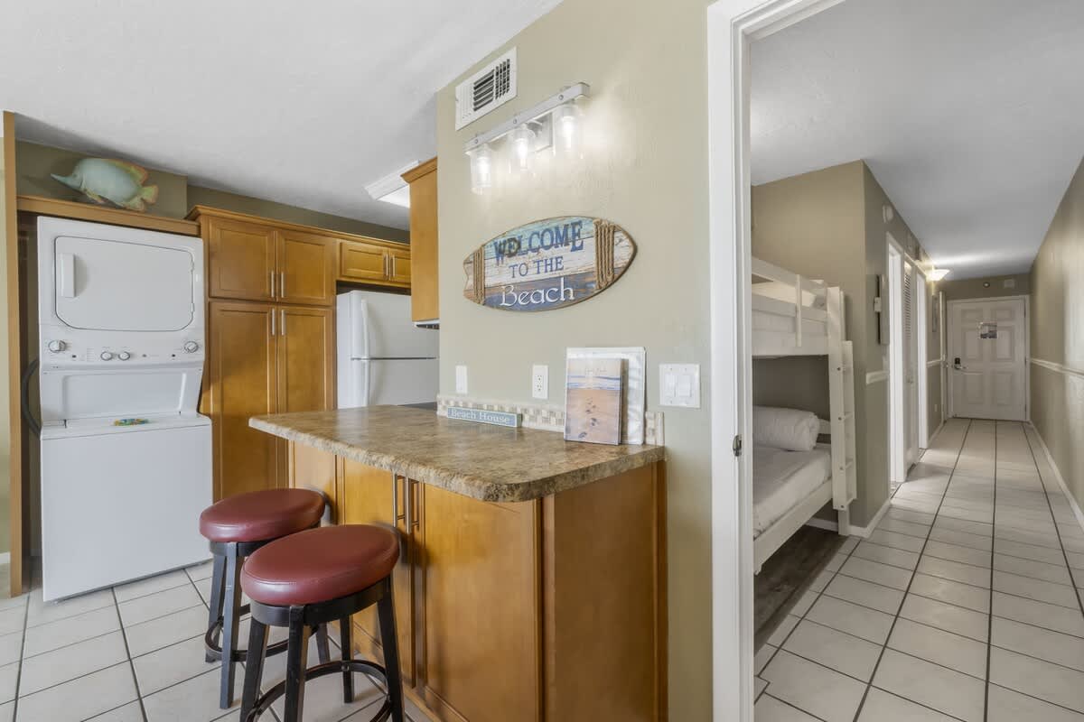 The Summit 1128 – Beach-themed kitchen area with bar stools, laundry appliances, and hallway leading to a bunk bed room.