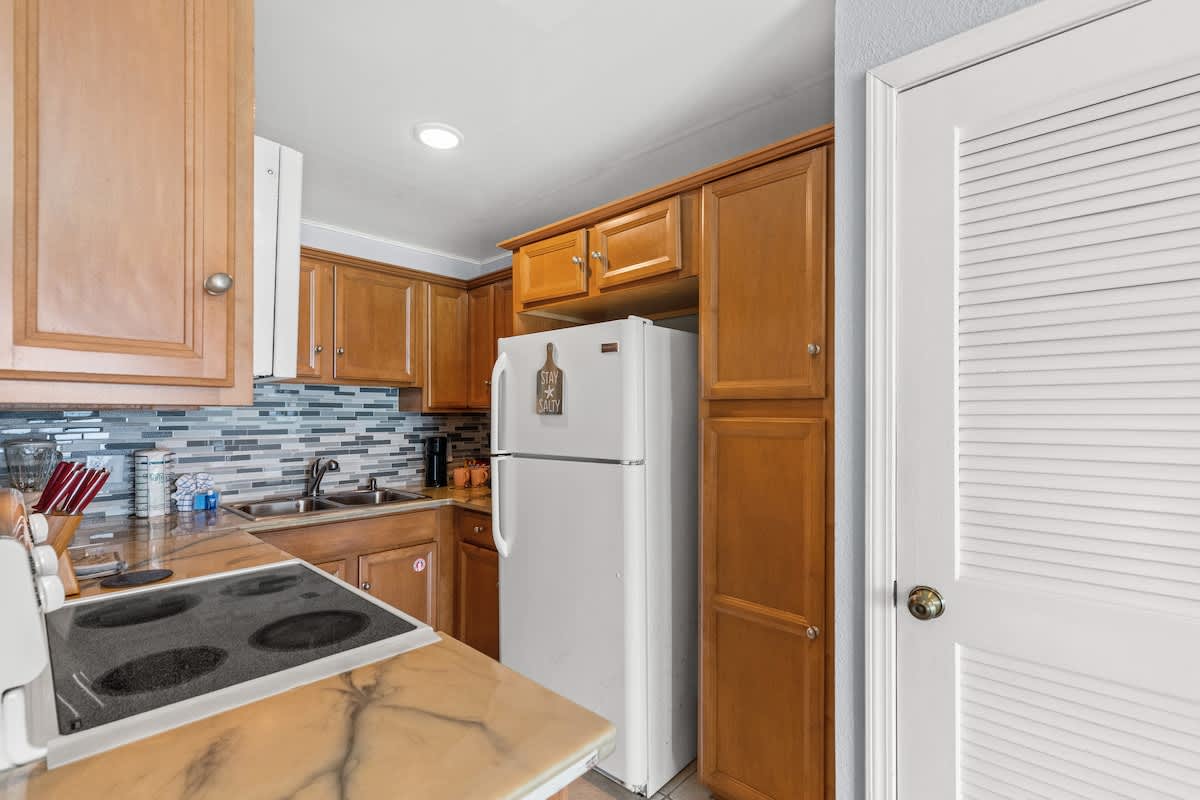 The Summit 1409 – Kitchen with wooden cabinets, white refrigerator, and tiled backsplash over a countertop with a stove.