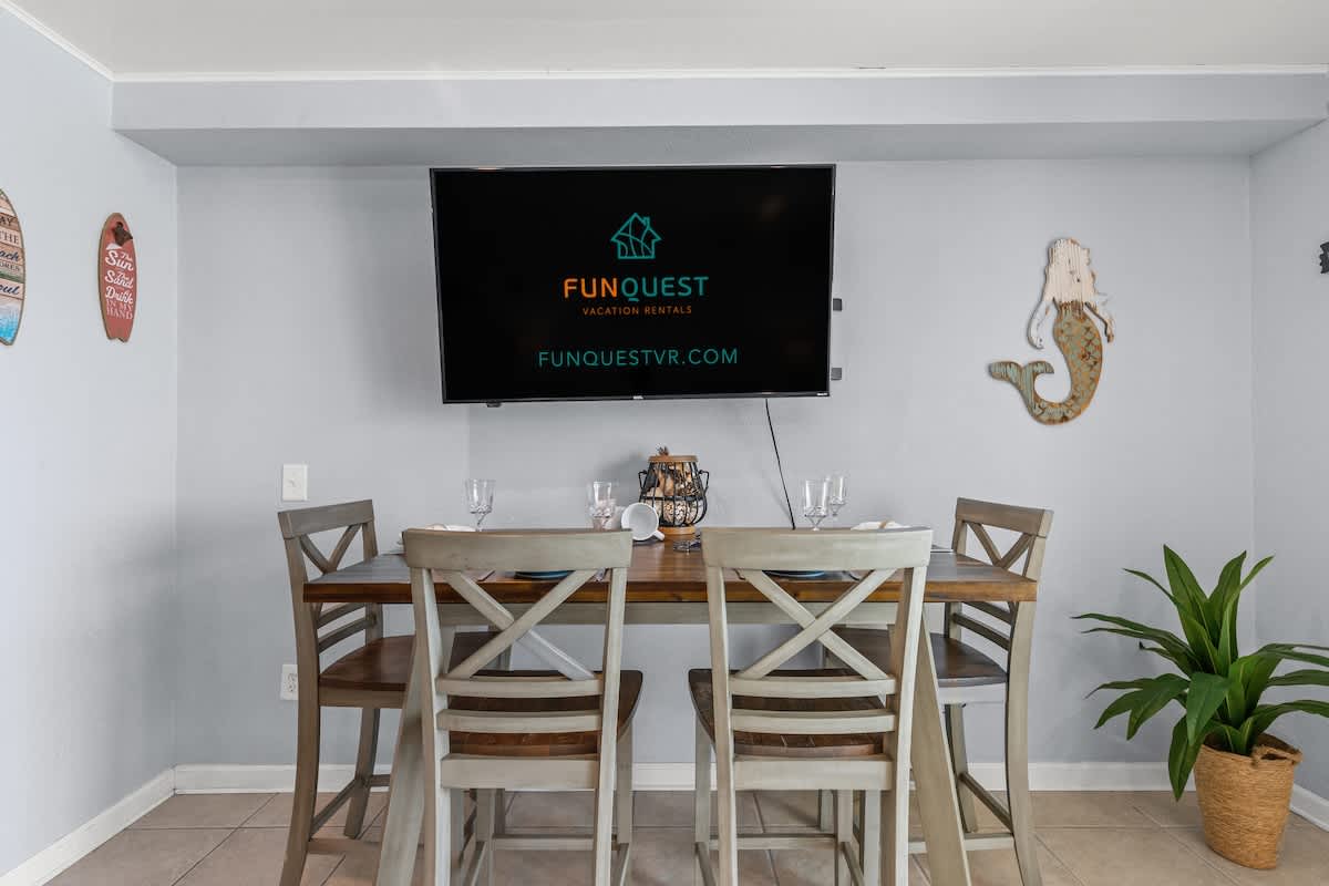 The Summit 1409 – Dining area with a wooden table, four chairs, a wall-mounted TV, and decorative wall art.