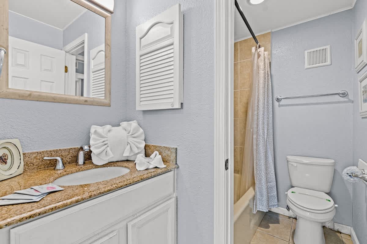 The Summit 1409 – Bathroom with a granite countertop, sink, shower, and toilet. Light blue walls and decorative towels.